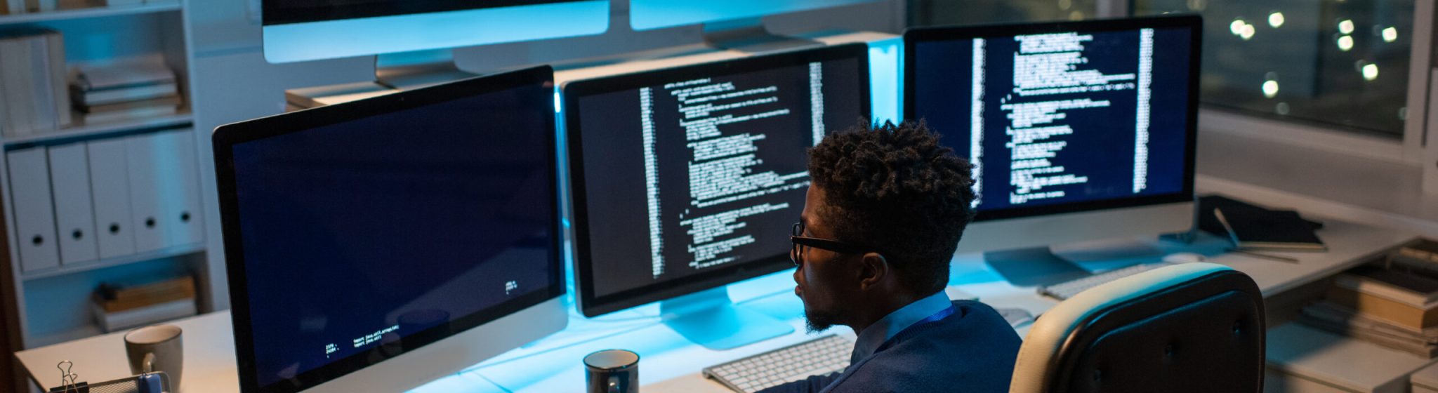 Young contemporary software developer working with decoded data while sitting in front of computer monitor in office at night